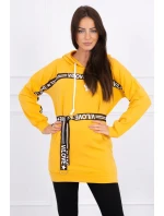 Šaty zdobené stuhou a nápismi v horčicovej farbe