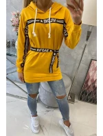 Šaty zdobené stuhou a nápismi v horčicovej farbe