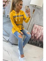 Šaty zdobené stuhou a nápismi v horčicovej farbe